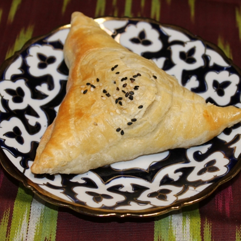 Golden triangular pastry topped with black and white sesame seeds on an ornate blue-and-white patterned plate.
