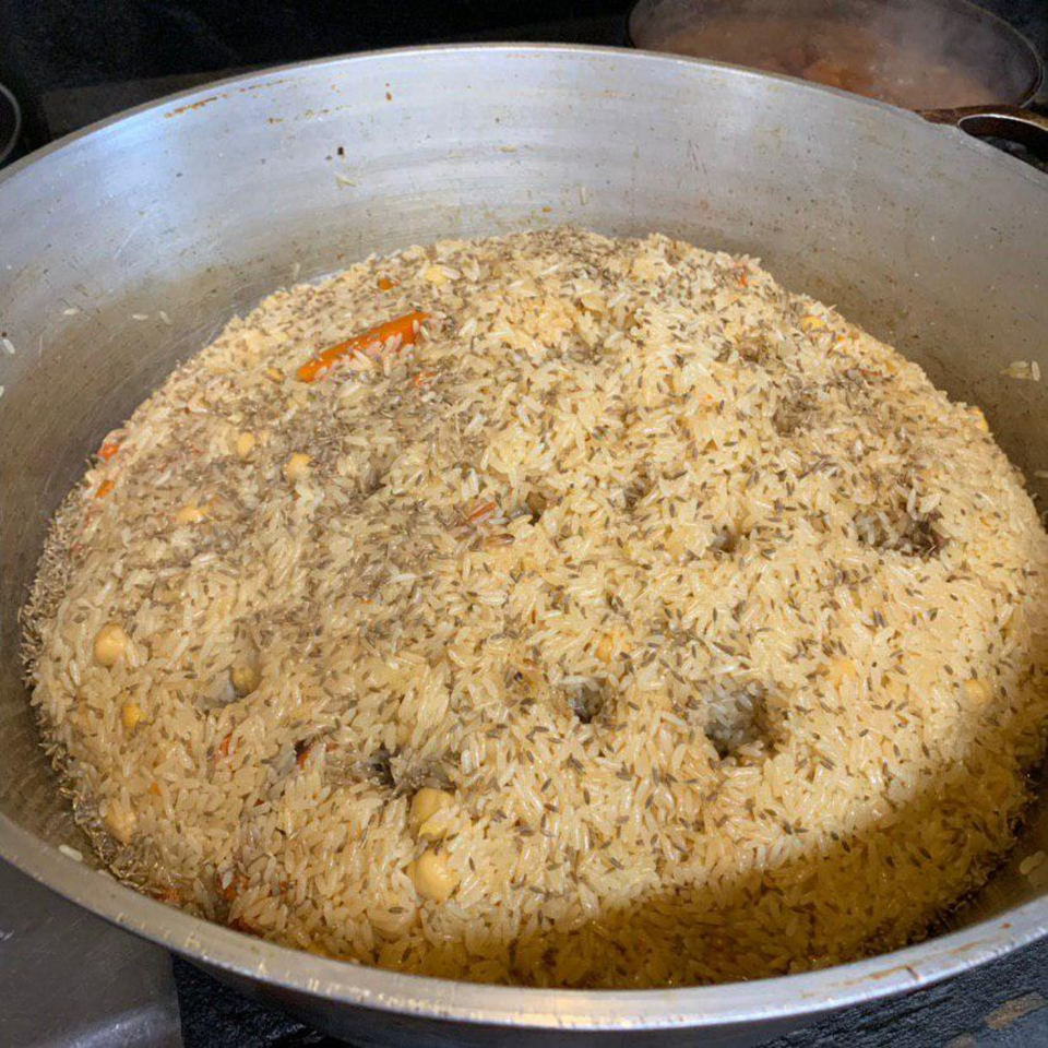Large pot filled with seasoned rice, carrots, chickpeas, and spices, prepared in a commercial kitchen.