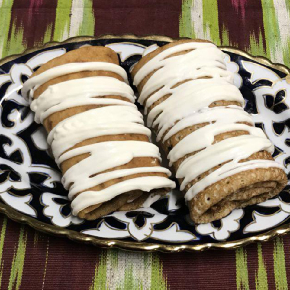 Two rows of golden cookies drizzled with white icing on an ornate black-and-white plate.