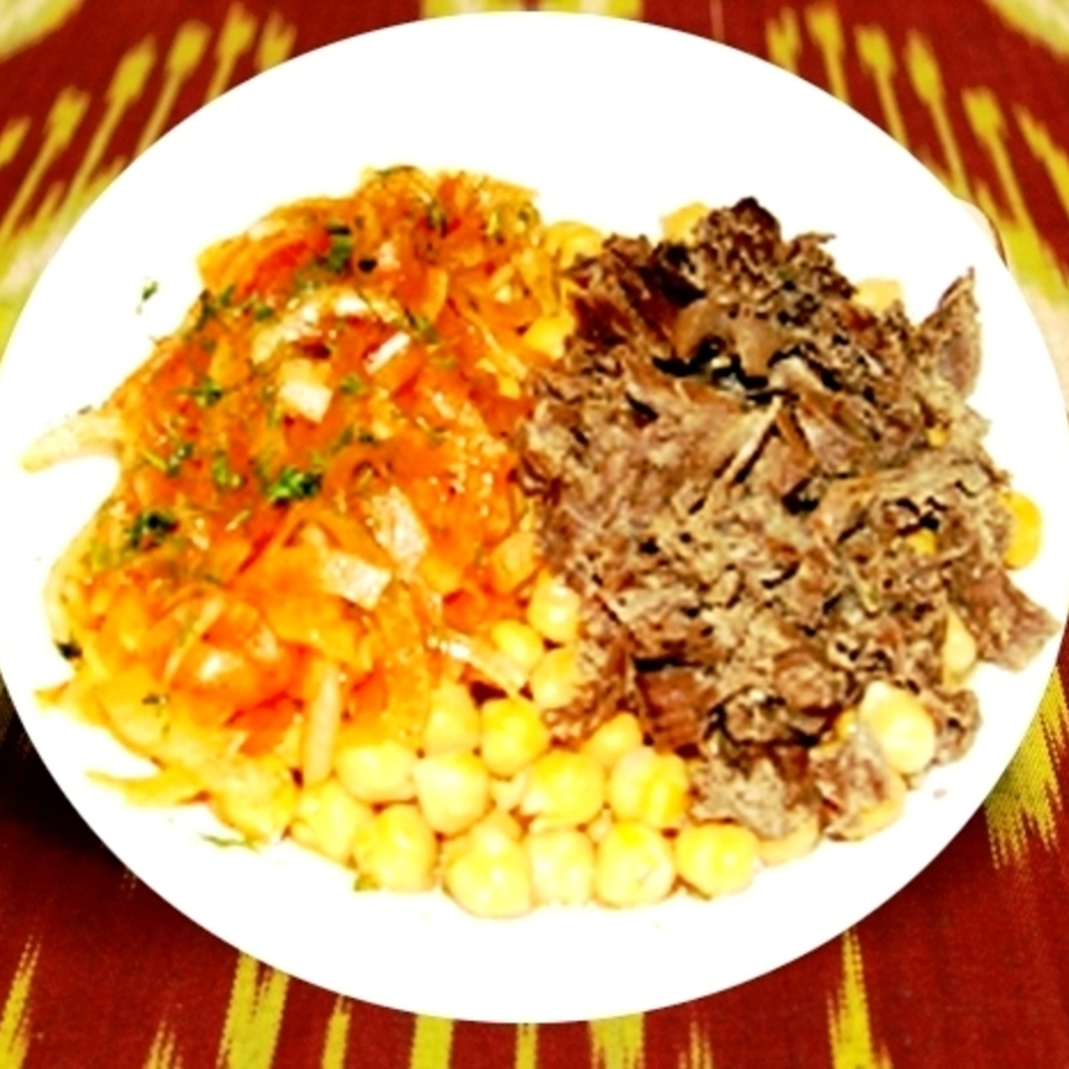 White plate with chickpeas, shredded meat, and orange vegetable salad on a red and yellow patterned tablecloth.