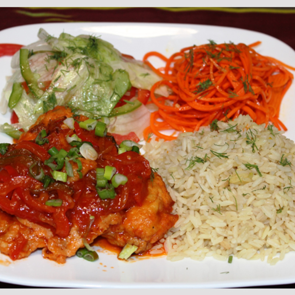 Plate of seasoned rice, shredded carrots, salad, and saucy chicken garnished with green onions and herbs.