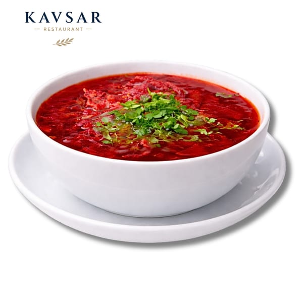 A white bowl of vibrant red borscht, garnished with fresh green herbs, on a white saucer.