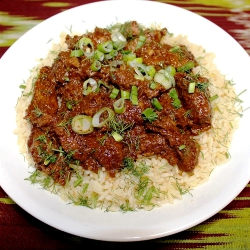 A white plate of rice topped with richly spiced meat, green onions, and fresh dill.