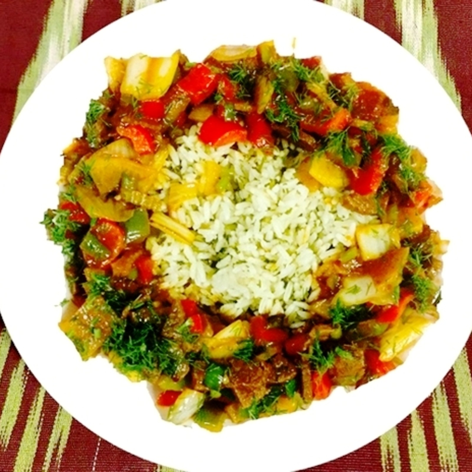 White rice surrounded by colorful sautéed vegetables, herbs, and red peppers on a white plate.