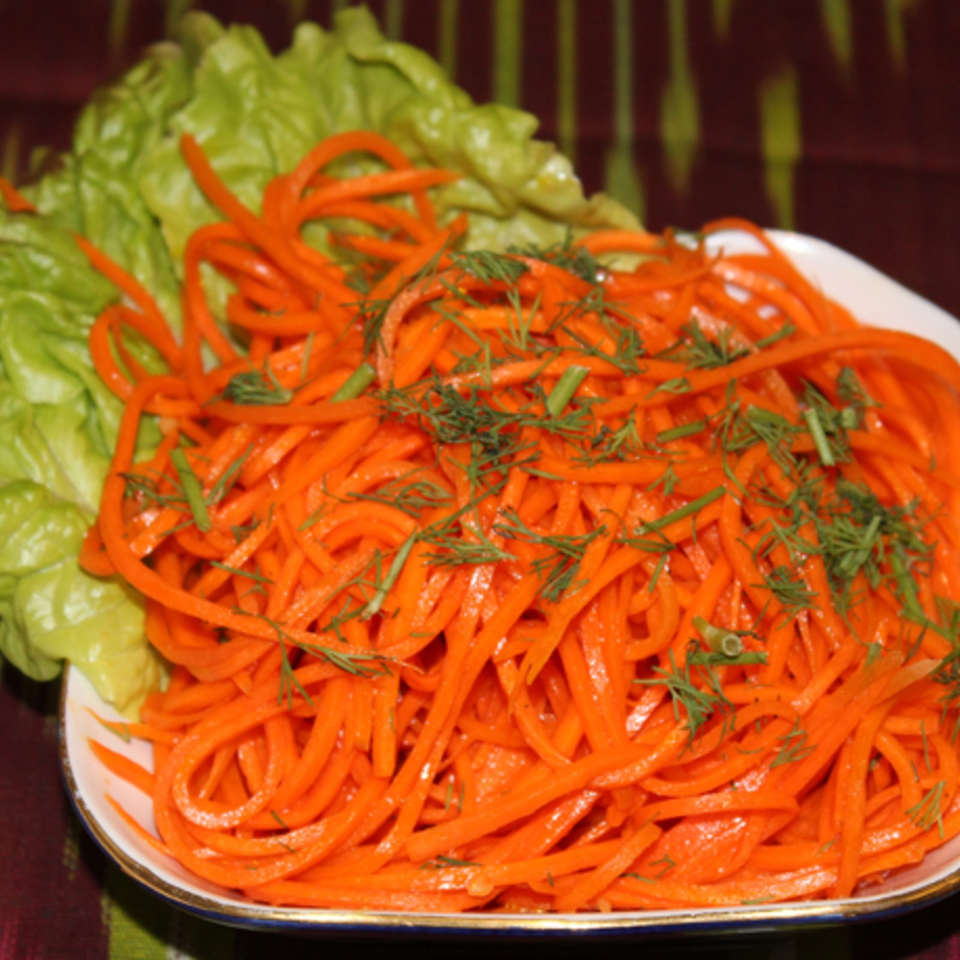 Plate of shredded carrot salad garnished with fresh dill and served on a bed of lettuce.