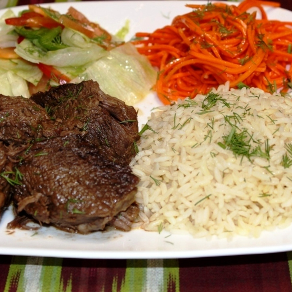 Grilled steak served with herbed white rice, shredded carrots, and fresh lettuce salad on a rectangular plate.