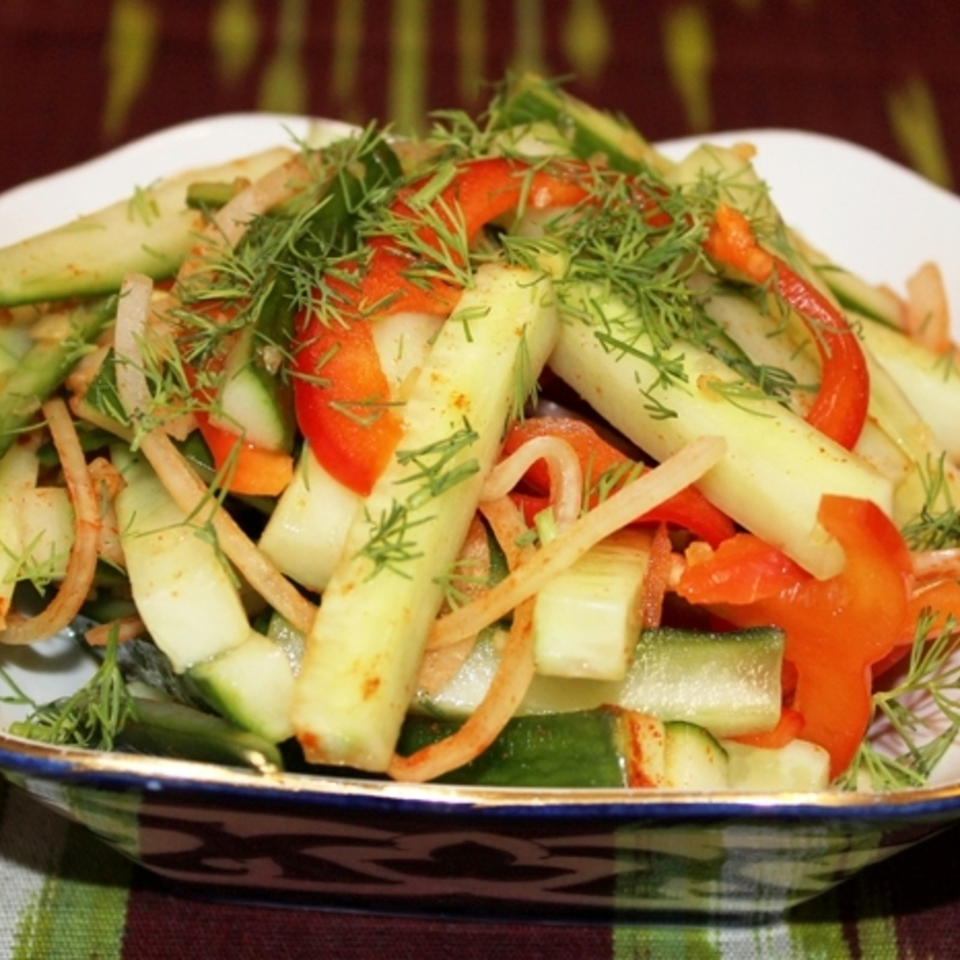 Colorful cucumber and red pepper salad topped with fresh dill, served in a decorative bowl.
