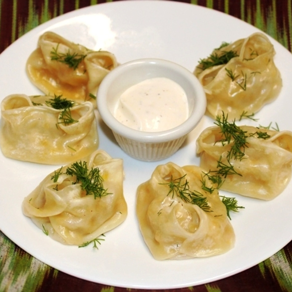 Plate of steamed dumplings garnished with dill surrounding a bowl of creamy dipping sauce.