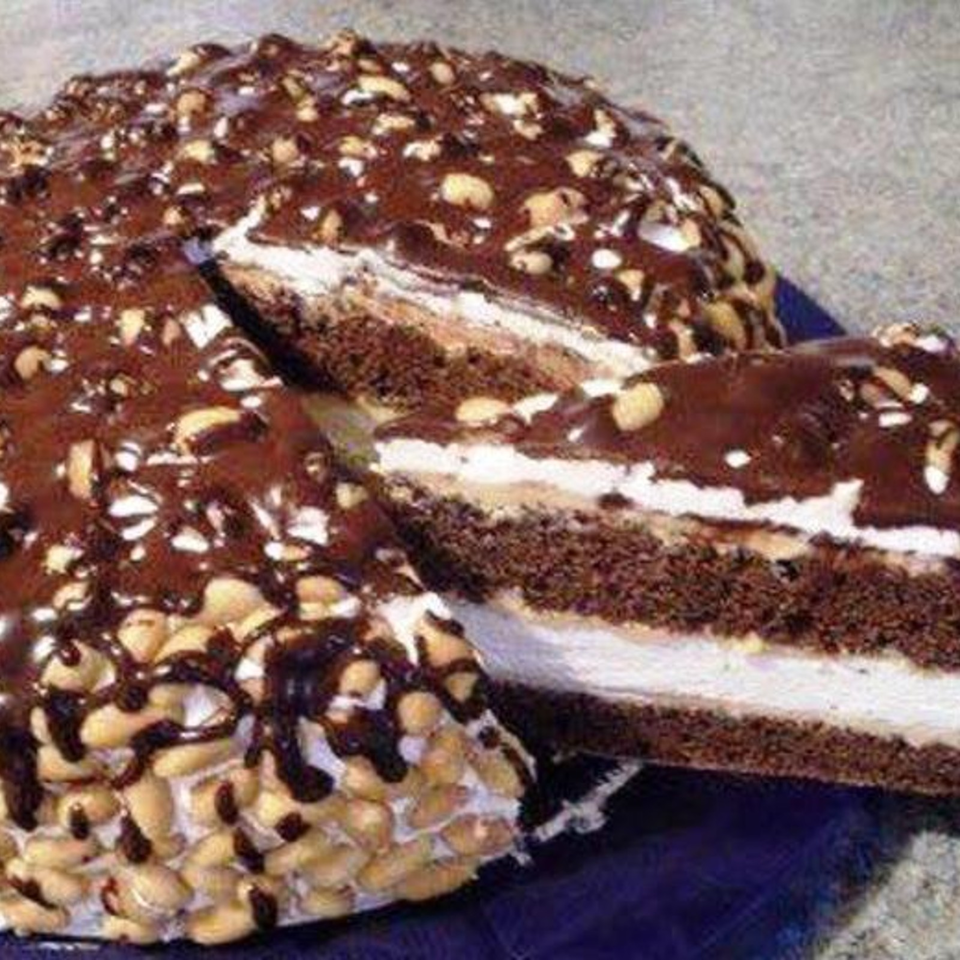 Chocolate cake with white cream filling, chocolate glaze, and chopped nuts on top and around the sides.