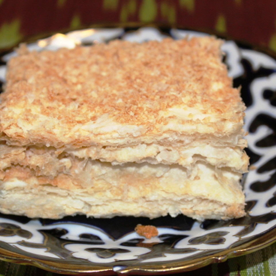 Layered golden pastry topped with crisp crumbs, served on an ornate black-and-white plate.