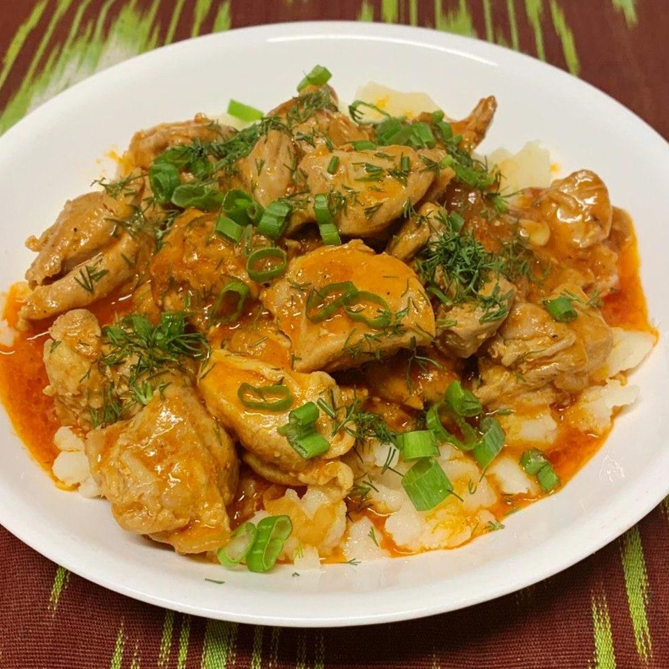 White plate of chicken pieces and rice covered in orange sauce, fresh dill, and chopped green onions.