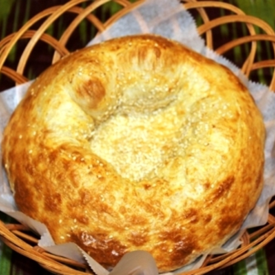 Golden-brown sesame-topped round bread loaf served in a woven basket lined with parchment paper.
