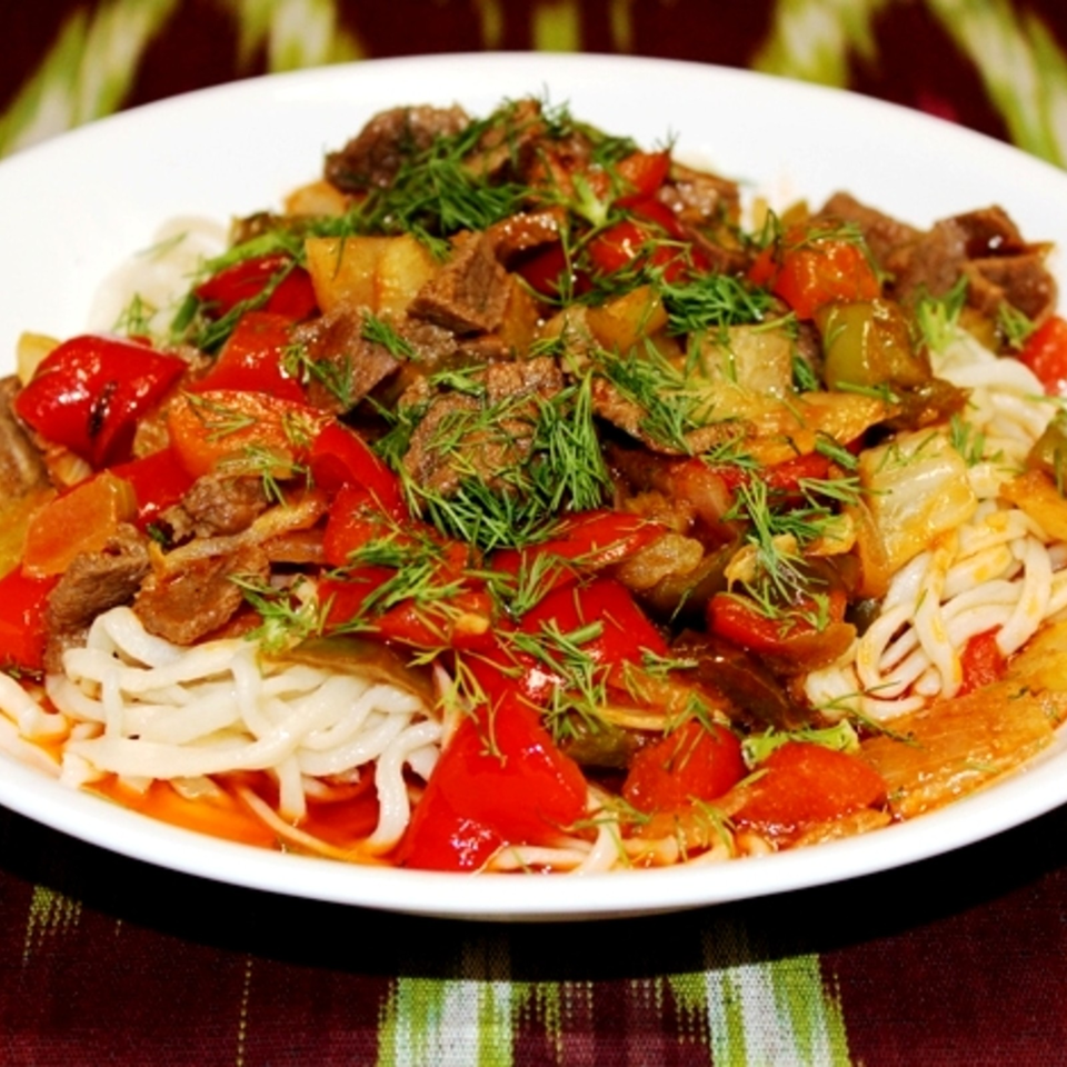 Plate of noodles topped with tender beef, roasted peppers, vegetables, and fresh dill.