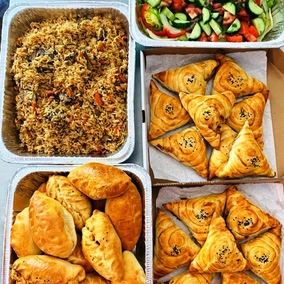 Trays of seasoned rice, fresh cucumber-tomato salad, golden sesame-topped pastries, and assorted baked savory breads.