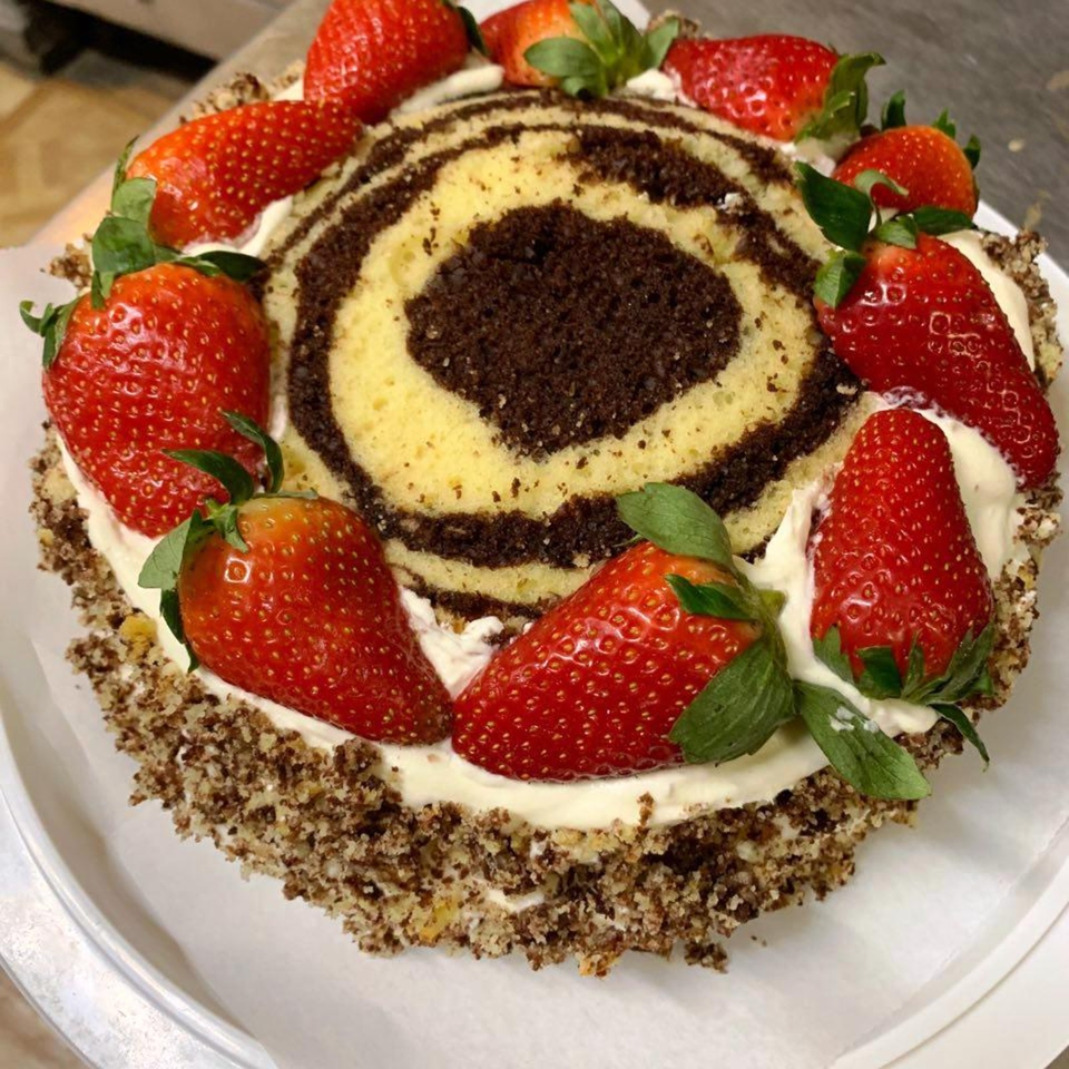 Round chocolate-and-vanilla cake topped with whipped cream and fresh strawberries, featuring a spiral-patterned center.