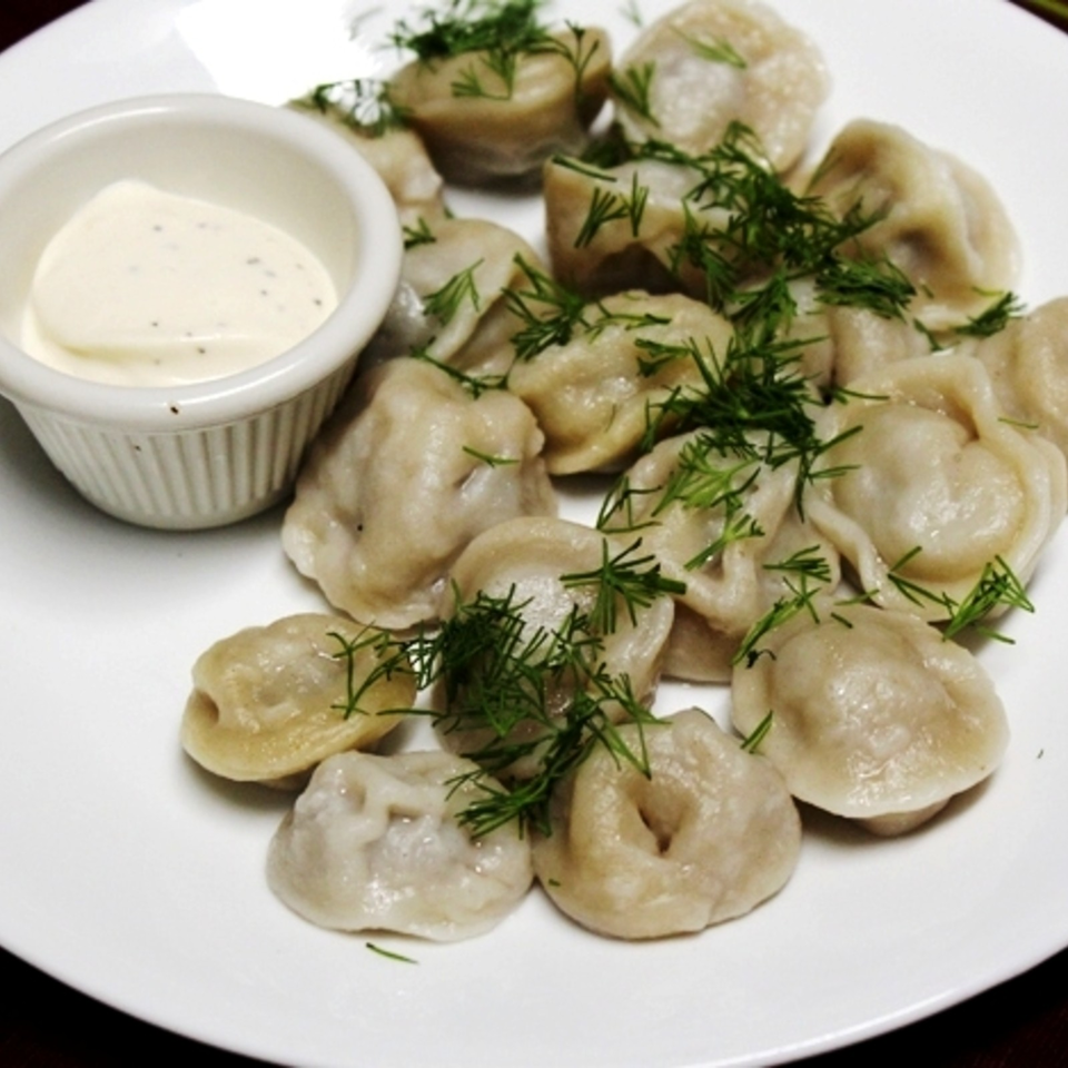Plate of dumplings garnished with fresh dill, served with a small bowl of creamy dipping sauce.