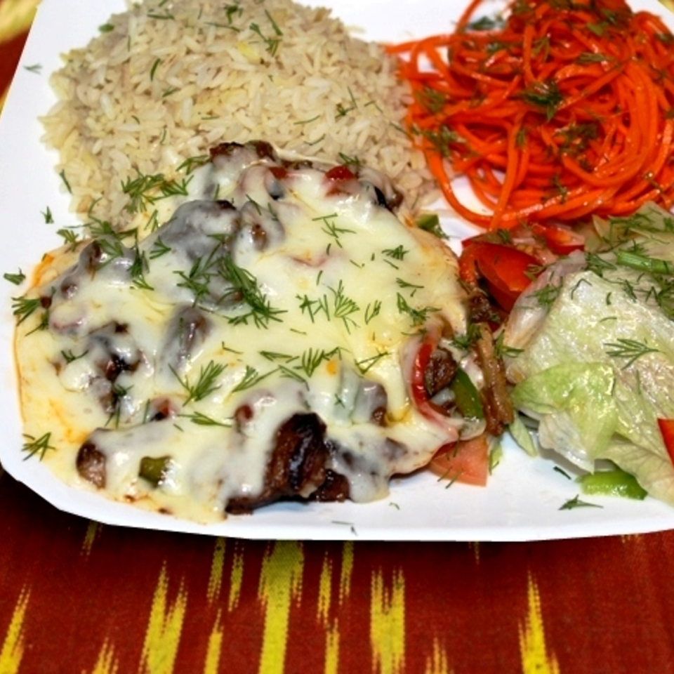 Plate of cheesy grilled meat topped with dill, served with seasoned rice, shredded carrots, and salad.