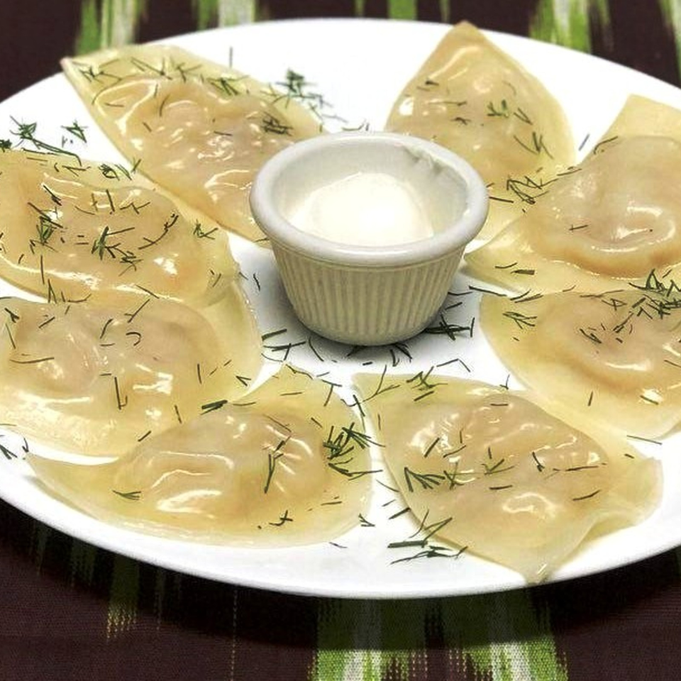 Plate of translucent dumplings garnished with dill surrounding a small cup of creamy dipping sauce.