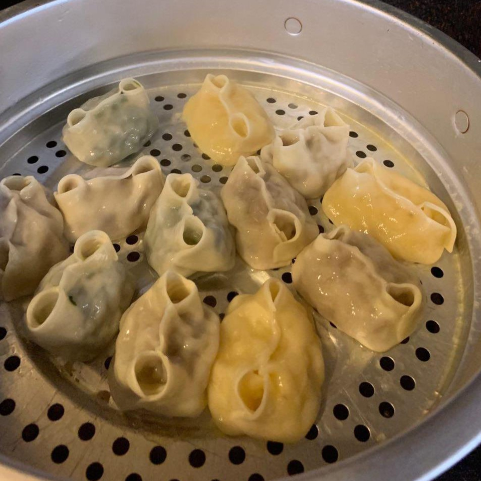 Steamed dumplings in assorted pale and yellow wrappers arranged in a perforated metal steamer basket.