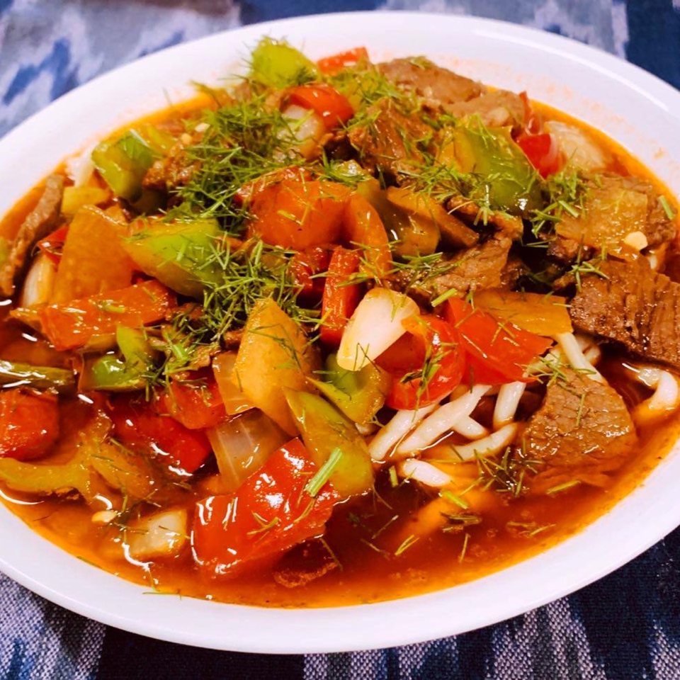 Colorful beef and vegetable stew with tomatoes, peppers, onions, and fresh herbs served in a white bowl.