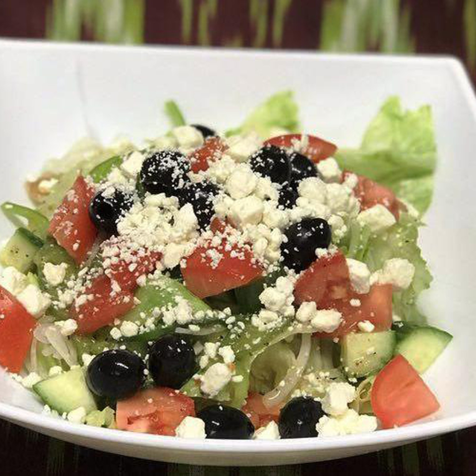 Greek salad with lettuce, tomatoes, cucumbers, black olives, and crumbled feta cheese served in a white bowl.