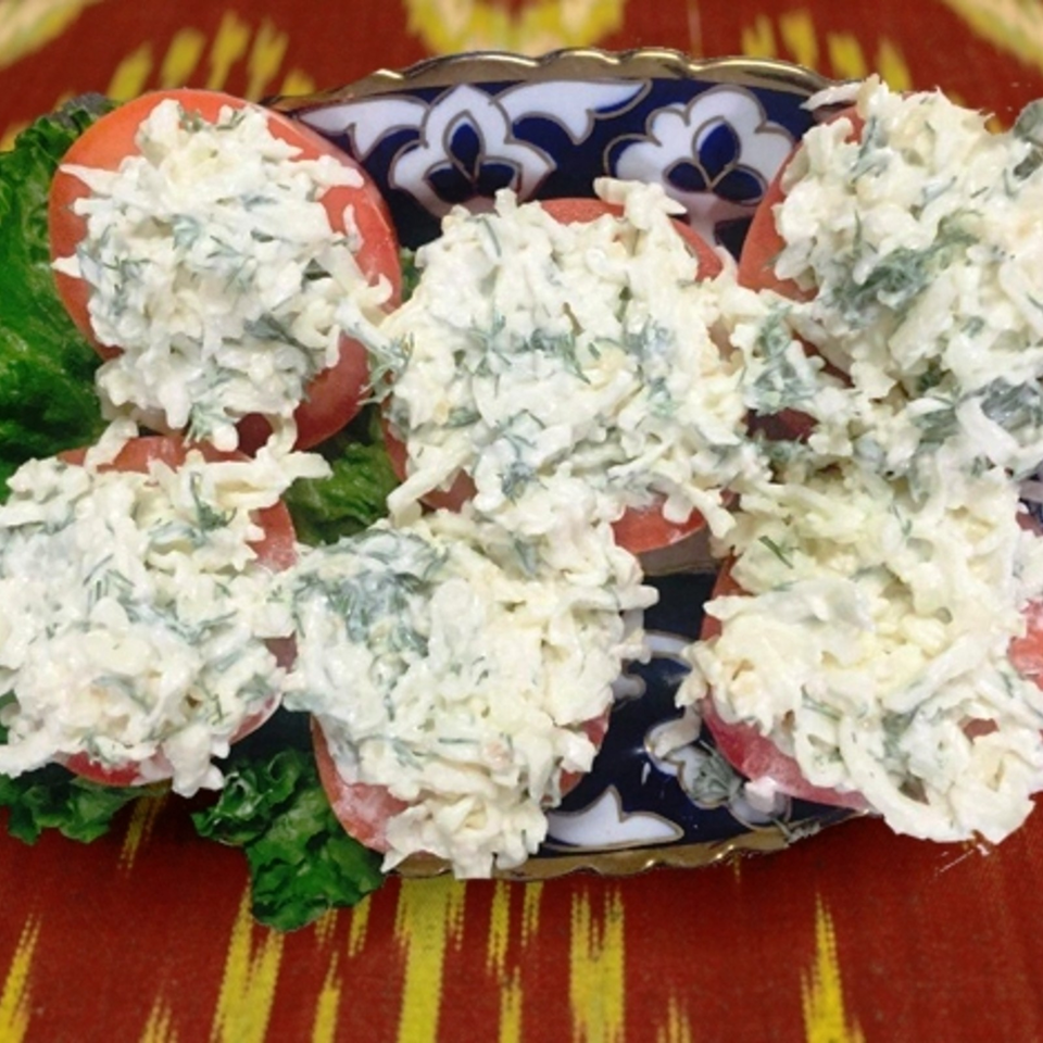 Tomato halves topped with creamy herb salad arranged on lettuce over an ornate blue-and-white serving plate.