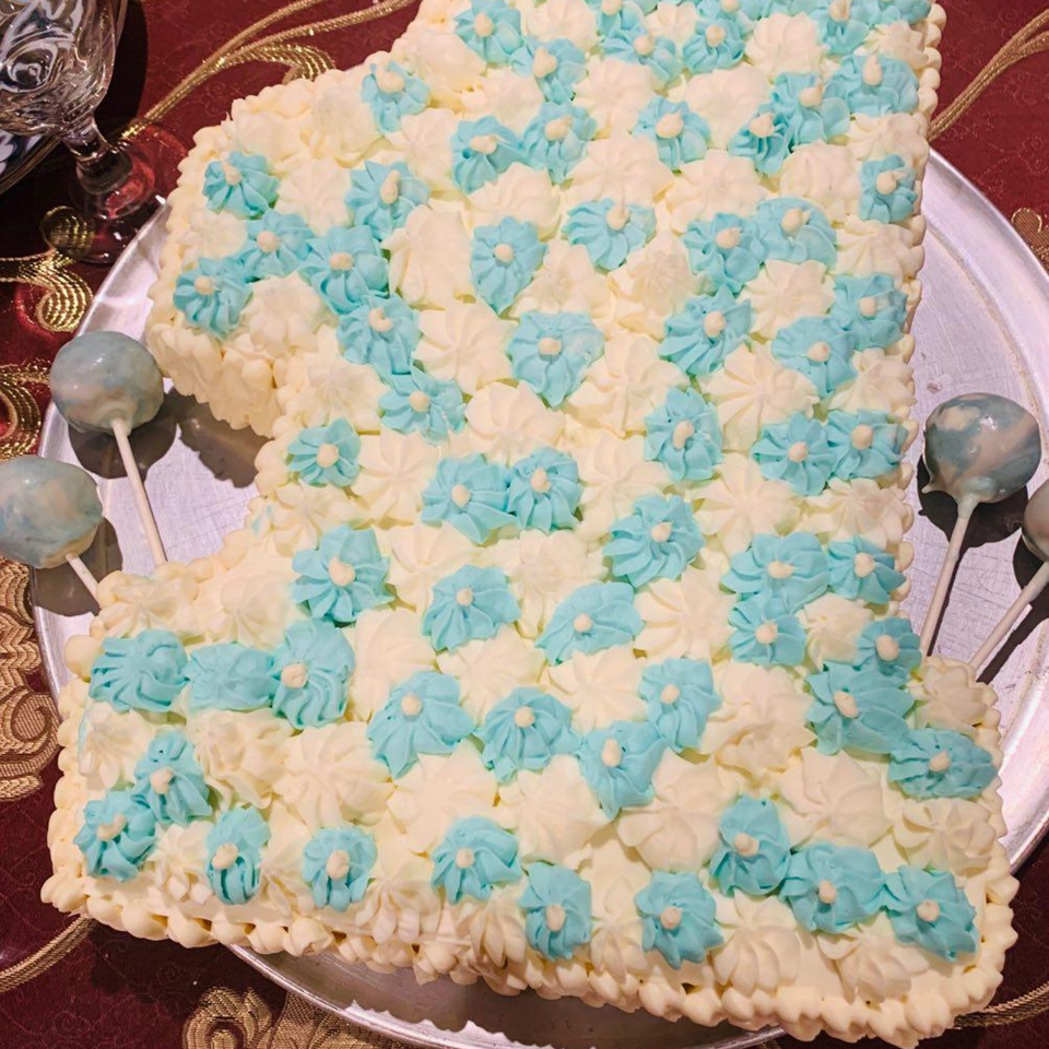 Rectangular cake covered with white and blue piped frosting flowers on a silver platter, surrounded by chocolate-coated cake pops.