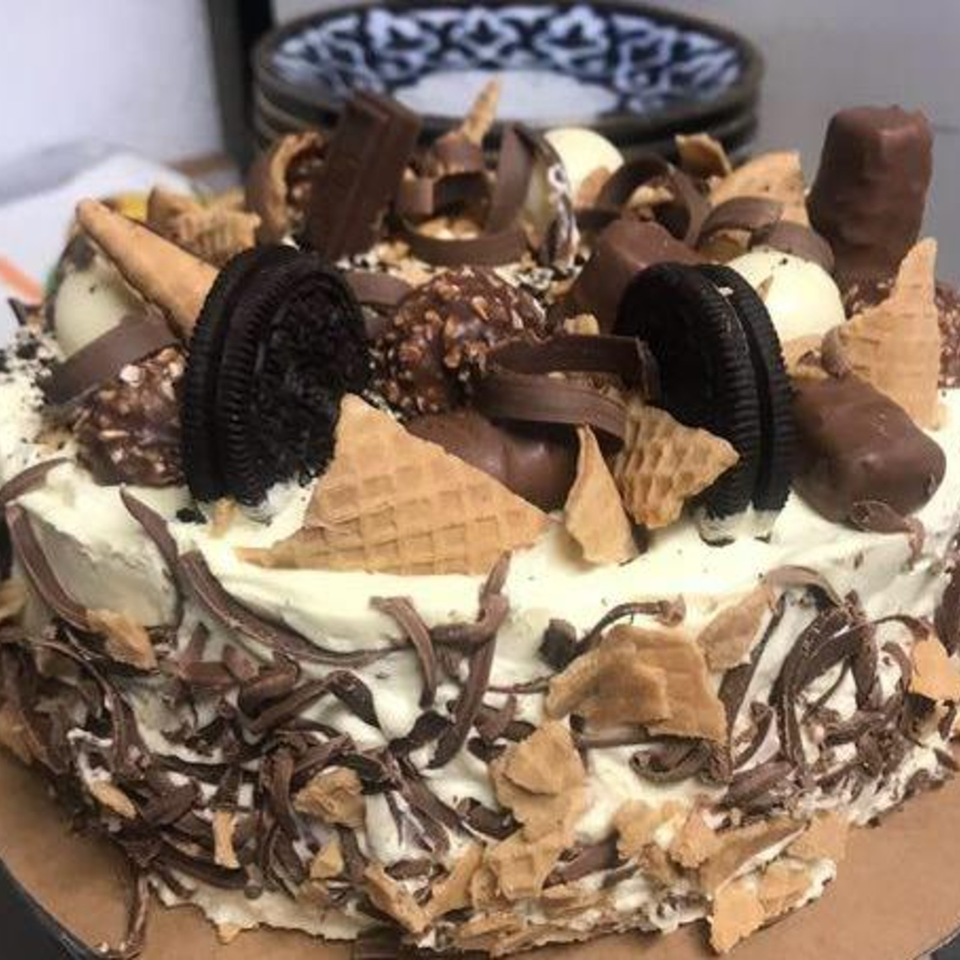 Chocolate-covered ice cream cake topped with cookies, wafer pieces, chocolate bars, and assorted candy.