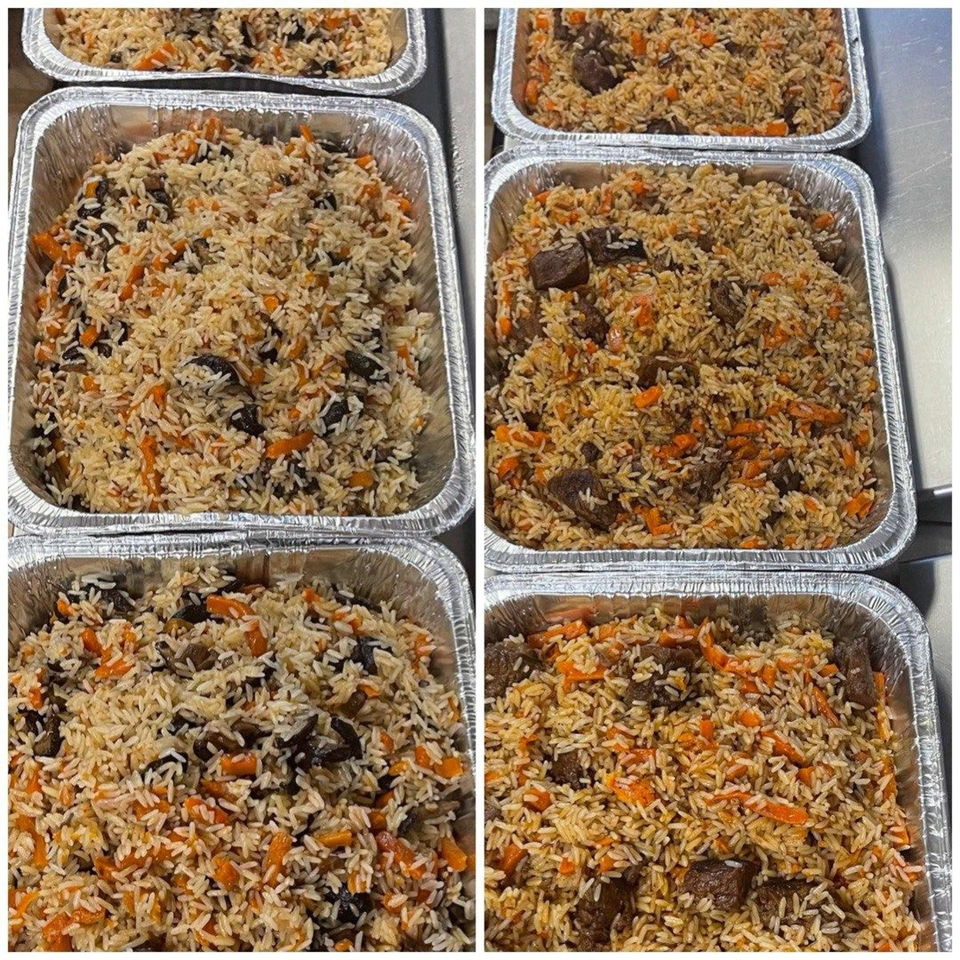 Aluminum catering trays filled with seasoned rice, carrots, dark beans, and chunks of meat.